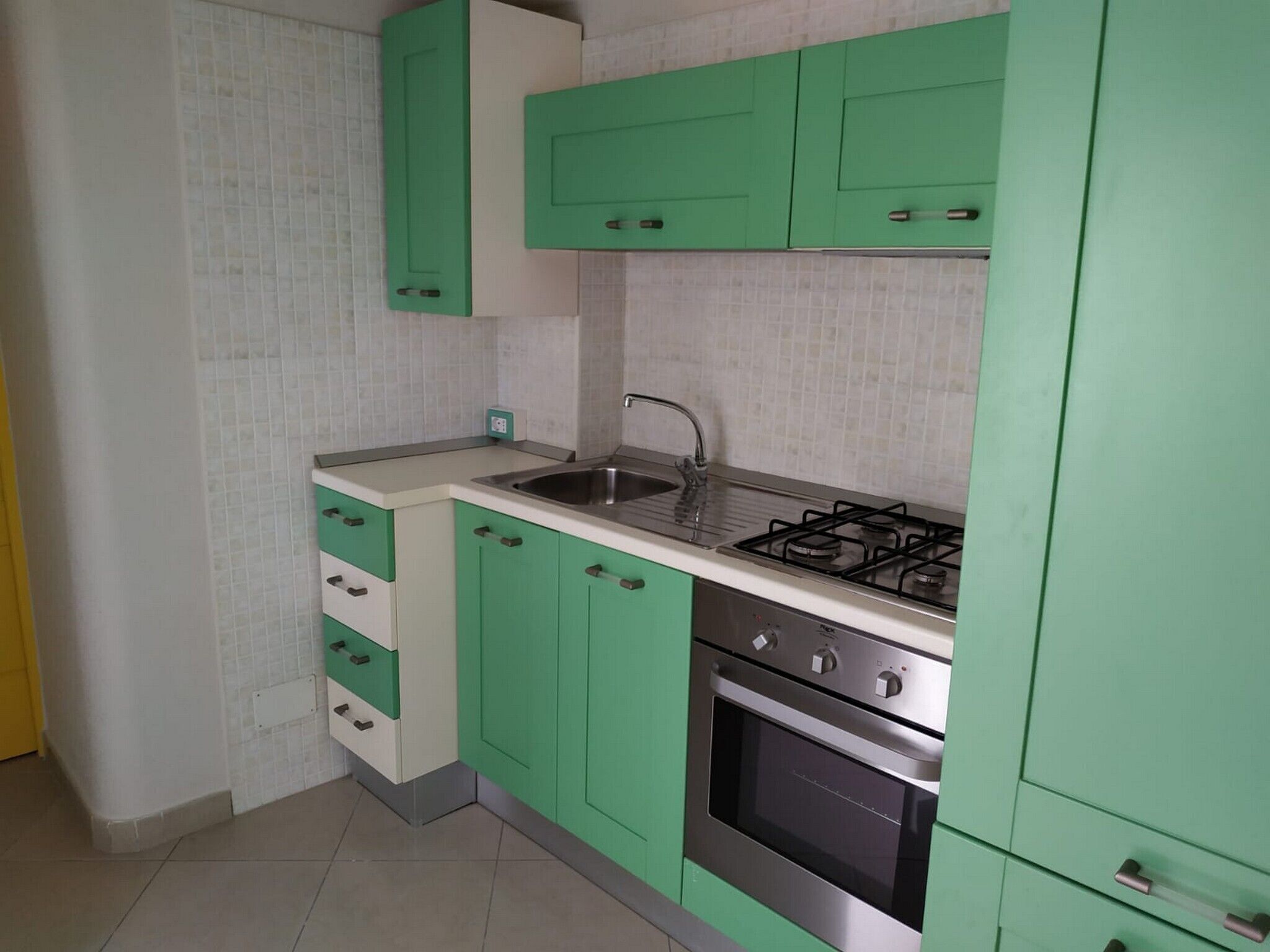 Una cocina con armarios verdes, un lavamanos de acero inoxidable y una estufa a gas.