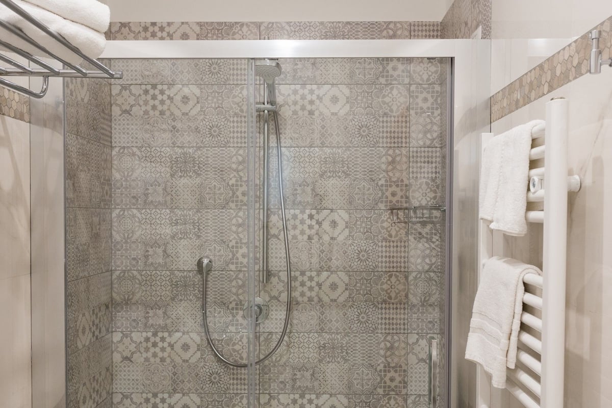 A shower with a glass door, patterned tiles, and a towel rack with towels.