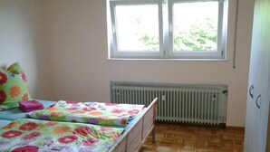 Ein kleines Schlafzimmer mit zwei Einzelbetten, einem Heizkörper und einem Fenster mit Blick auf Grünfläche.