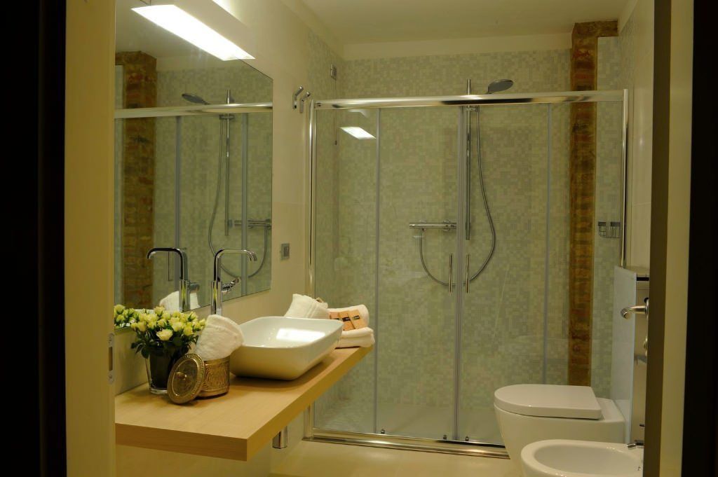 A modern bathroom with a glass-enclosed shower, a white sink with a bowl, and a toilet.