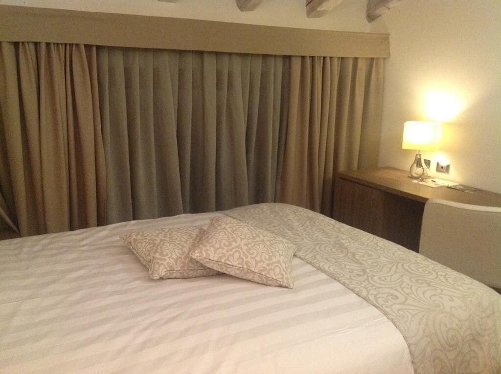 A hotel room with a bed, curtains, a nightstand, and a lamp.