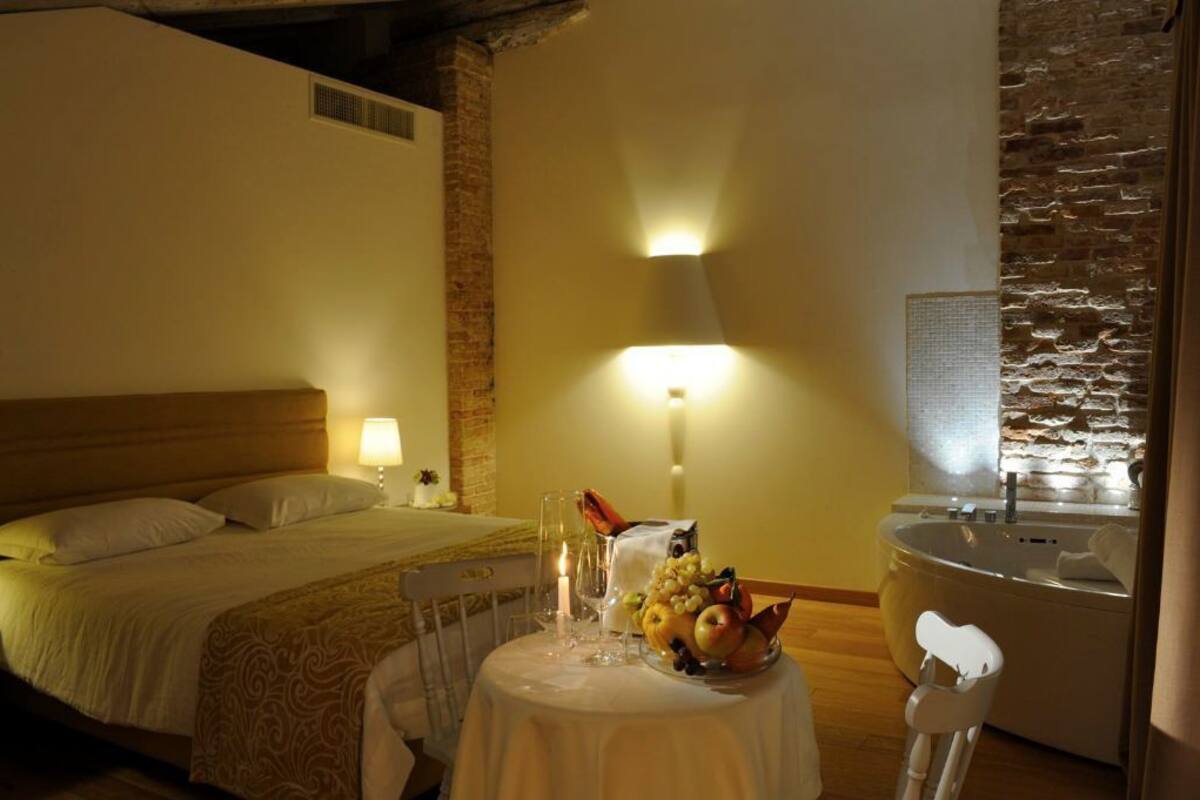 A hotel room with a bed, a table with fruit and a candle, a lamp, and a bathtub.