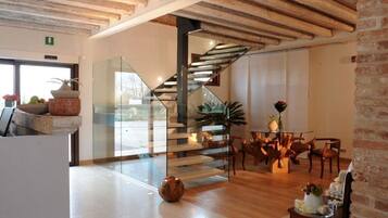 Un interno moderno con una scala in legno, ringhiere in vetro e un'area pranzo con sedie e tavolo in legno.