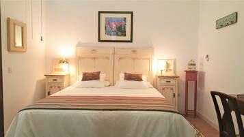 A double bed with a striped bedspread, two bedside tables with lamps, a framed picture on the wall, and a small table with a birdcage.