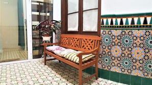 A wooden bench with a cushion, a potted plant, and a patterned tile wall.