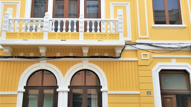 A multi-story building with yellow and white exterior walls, large windows, and a balcony with white balustrades.