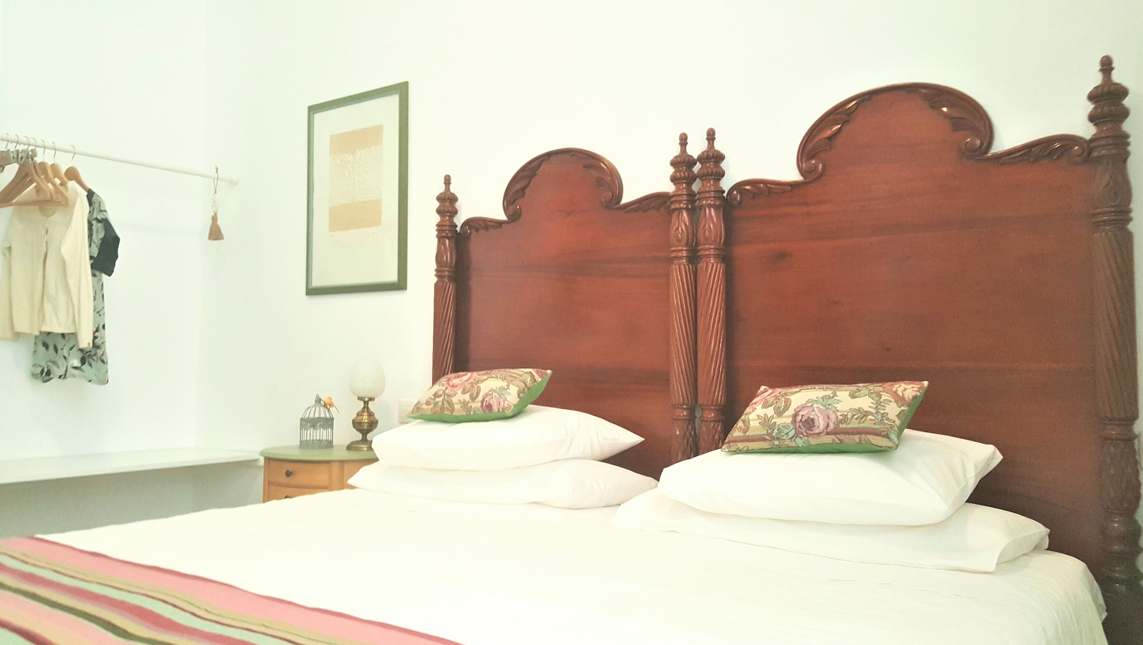 A bedroom with a wooden headboard, two white pillows, a striped blanket, a nightstand with a lamp, and a framed picture on the wall.