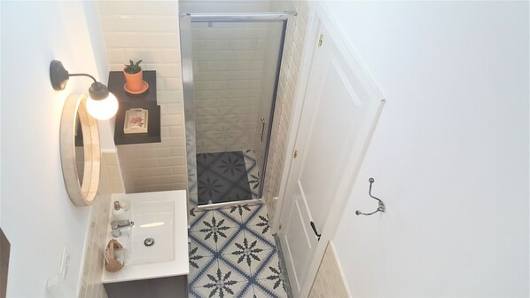 Un baño con un lavamanos blanco, un espejo, una planta en maceta y una ducha con puerta de cristal.