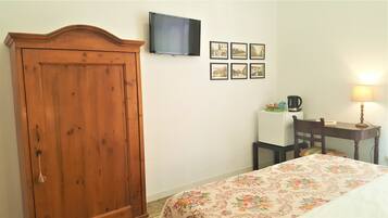 Una habitación con un armario de madera, un televisor en la pared, un escritorio con una lámpara y una cama con colcha estampada.