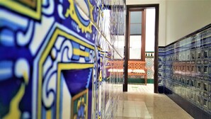 A hallway with intricate tile patterns on the walls and a view into a room with a patterned floor and a window.