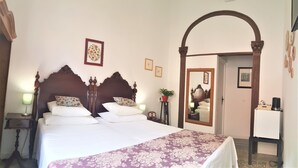 A bedroom with a large bed, a nightstand, a bedside lamp, a mirror, and a small table with a plant.