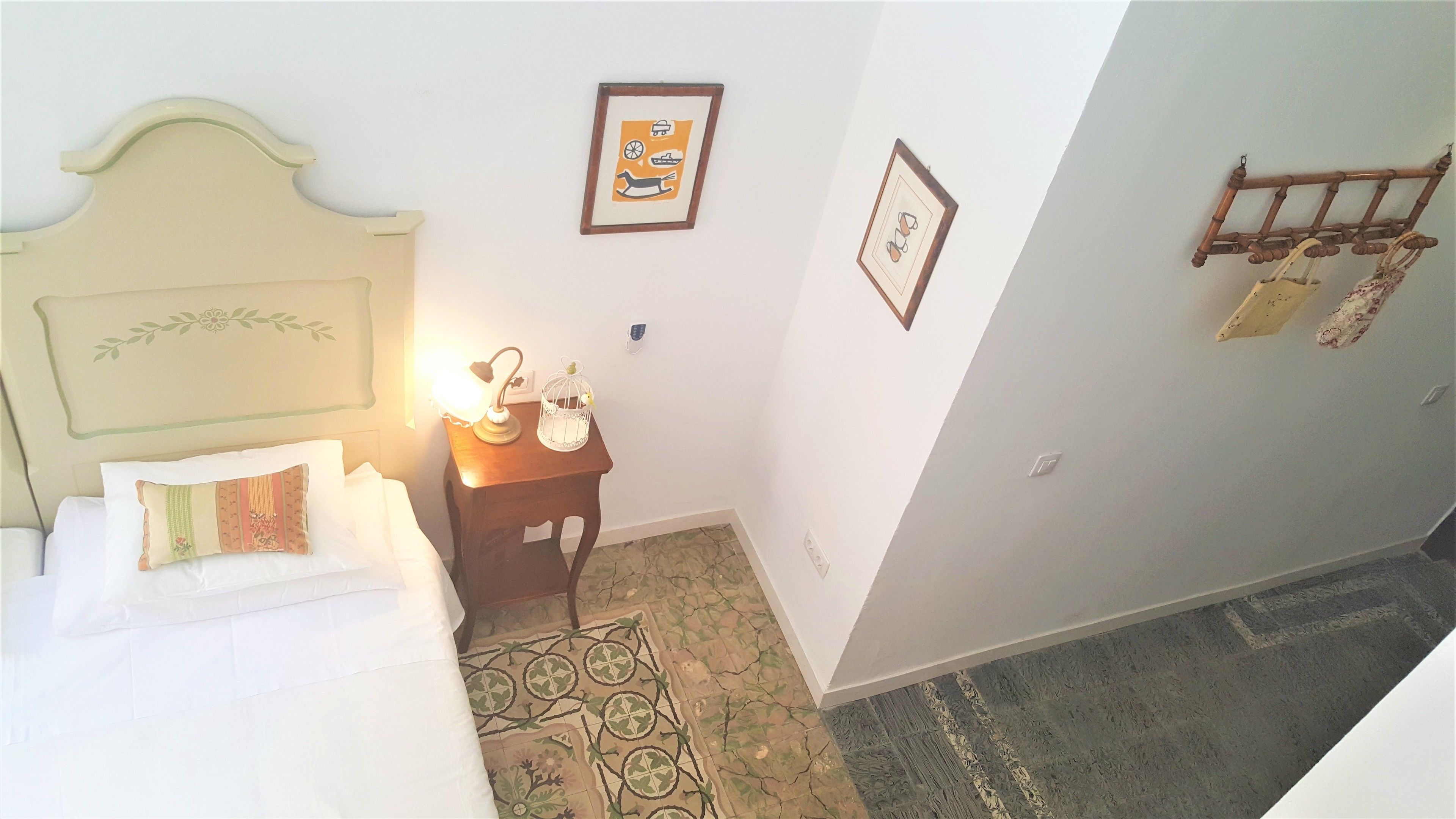 Quarto de hotel com uma cama, mesa de cabeceira com luminária, quadro emoldurado e cabideiro.