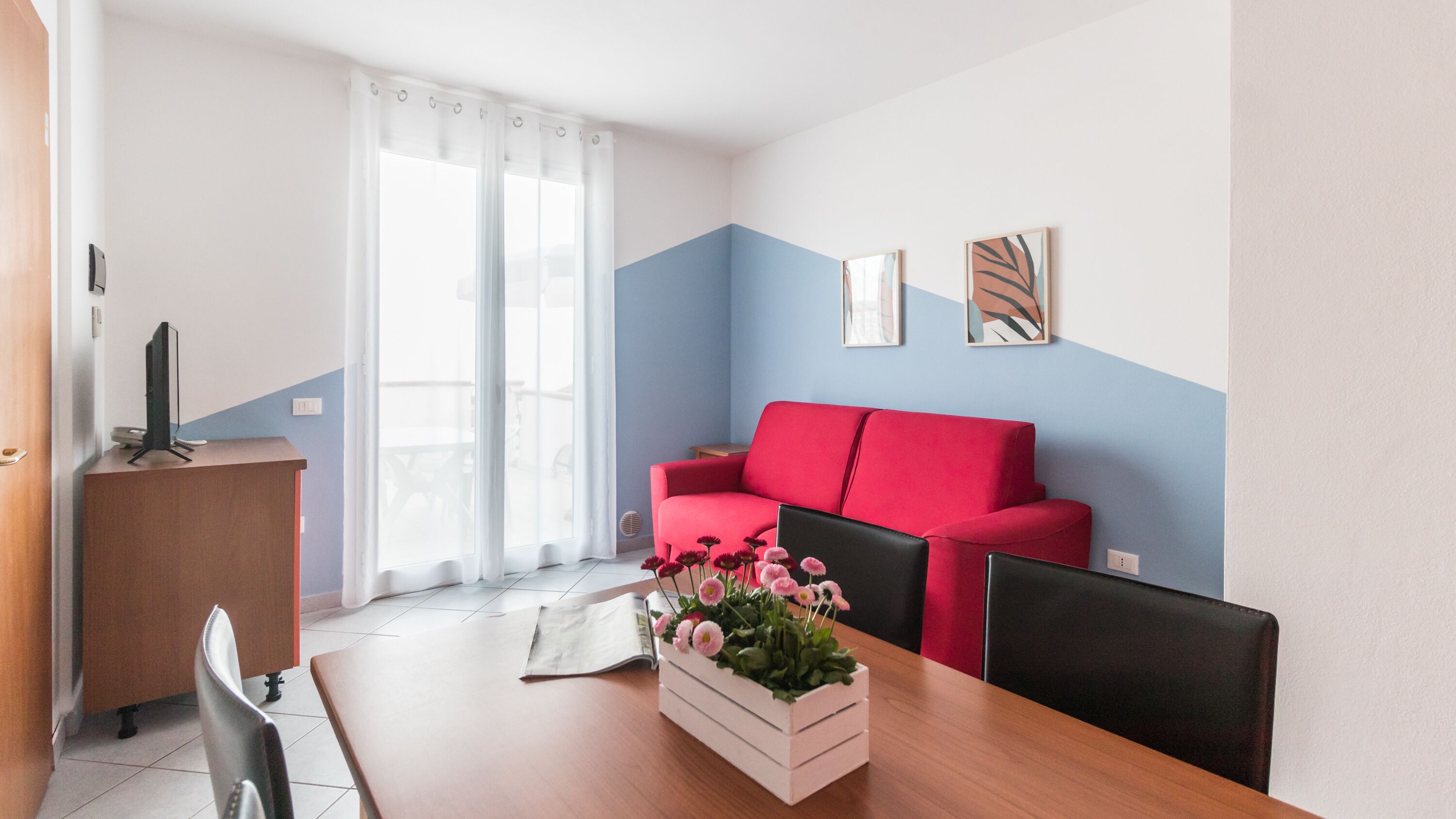 Una sala de estar moderna con un sofá rojo, una mesa de centro de madera y un arreglo floral blanco.