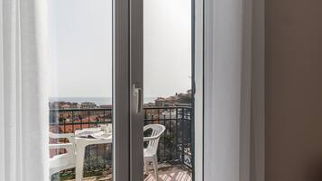 A balcony with a table and chairs, overlooking a cityscape with buildings and a body of water.