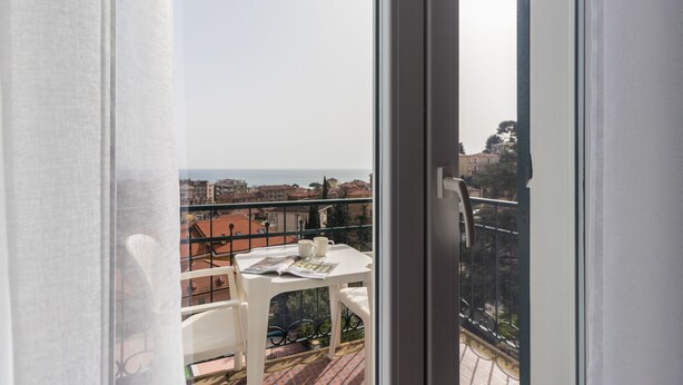 A balcony with a table, chairs, and a view of the city and sea. - Residence Il Poggio (Andora)