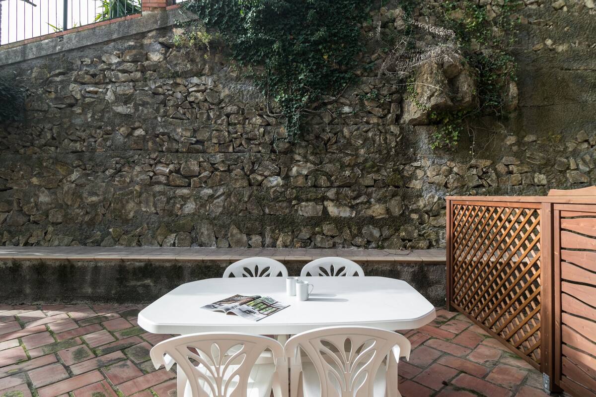 Un muro de piedra con una cerca de madera, una mesa blanca con sillas y un patio de ladrillo.