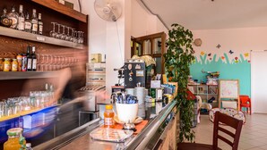 A bar area with shelves of liquor bottles and glasses, a fan, and a counter with a coffee machine and a plant. - Residence Il Poggio (Andora)