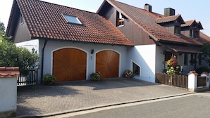 A two-story house with a tiled roof, two wooden garage doors, and a paved driveway. - Ferienwohnung Wagner (Altenthann)