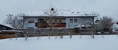 A two-story house with a wooden fence in front, surrounded by snow-covered trees.