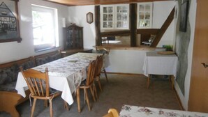 Un comedor con una mesa larga y varias sillas, un banco y una mesa pequeña con mantel blanco.