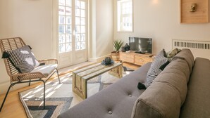 Olohuoneessa on sohva, puinen sohvapöytä, rottinkituoli, televisio ja seinällä oleva kello.
