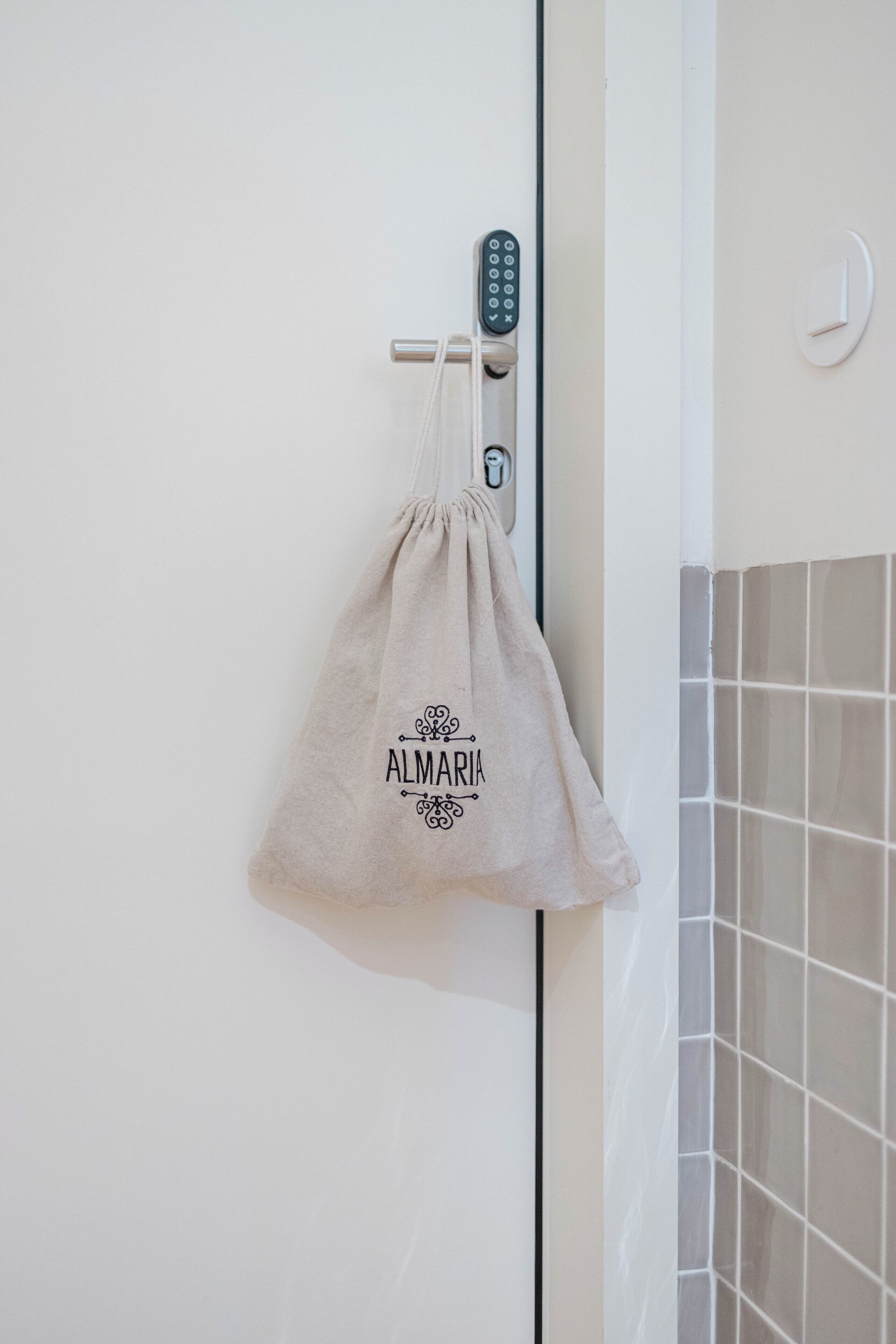 A bathroom with a towel hanging on a door handle, a wall clock, and a tiled wall.