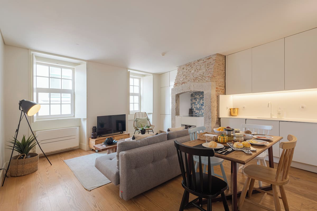 Un salon moderne avec un canapé gris, une table à manger avec des chaises, un téléviseur et une cheminée en pierre.