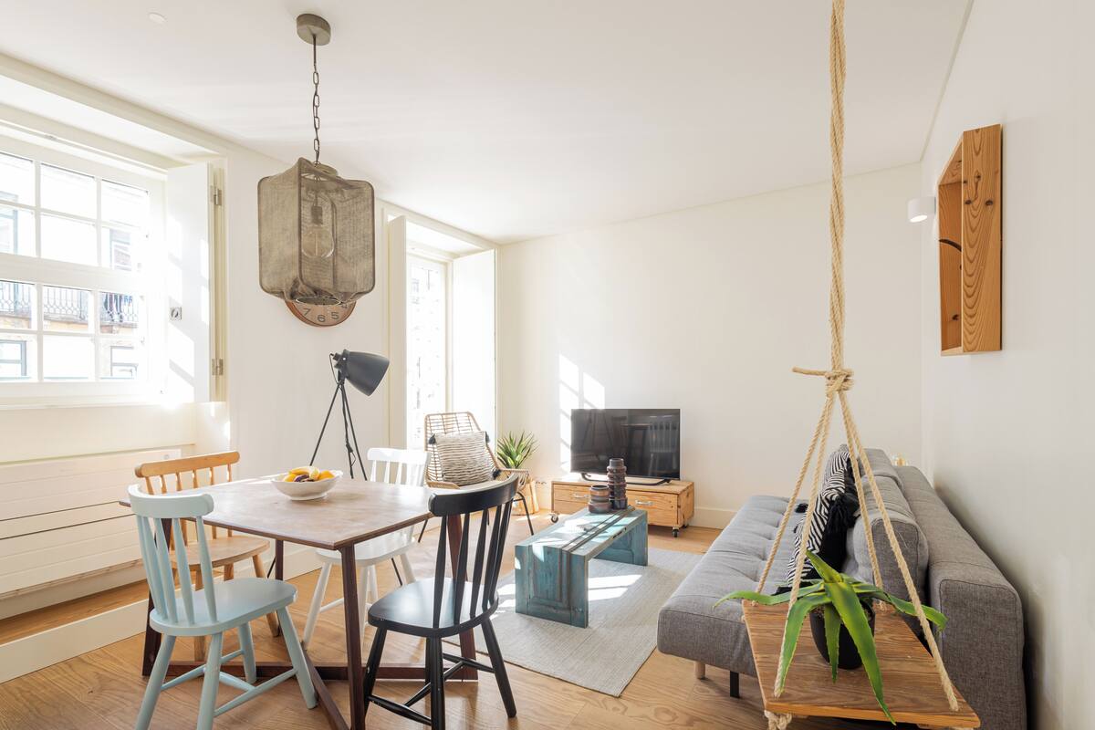 Un salon moderne comprenant un coin repas, un canapé, un téléviseur et une plante suspendue.