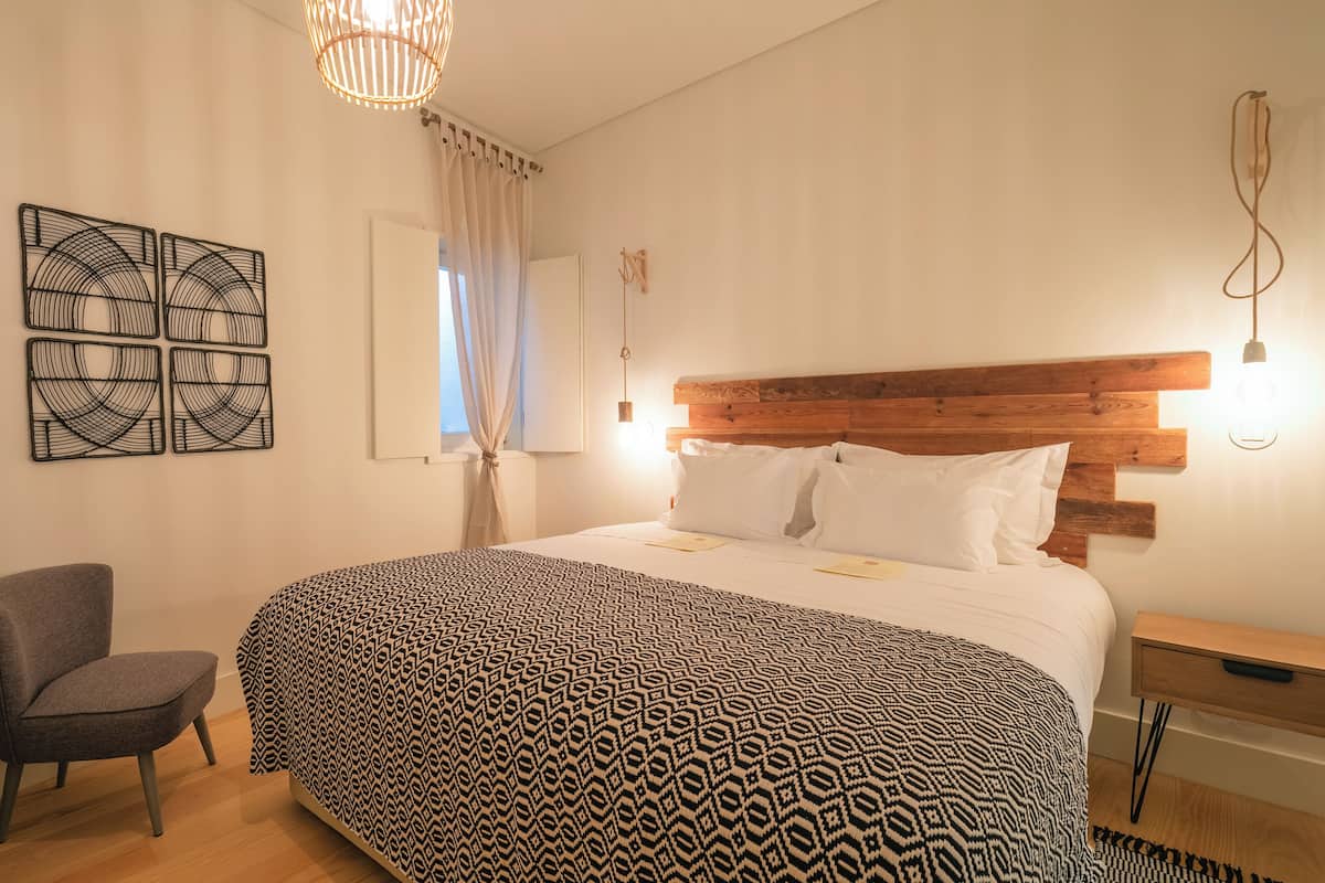Une chambre à coucher bien rangée, avec une couvre-lit à motifs, une tête de lit en bois, une table de chevet et une chaise.