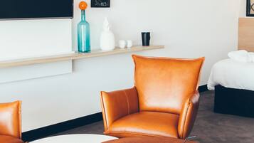 A modern hotel room with a brown leather chair, a white table, and a bed with white bedding.