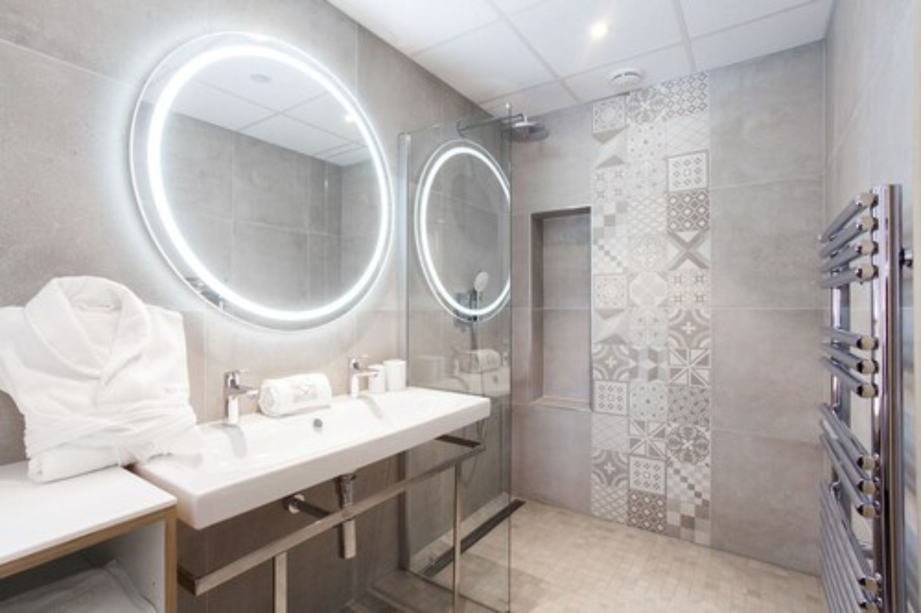 Un baño moderno con dos lavamanos, un espejo grande con luz circular y una zona de ducha.
