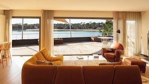 Un salón espacioso con un sofá grande, un sillón y vistas a un lago a través de amplias ventanas.