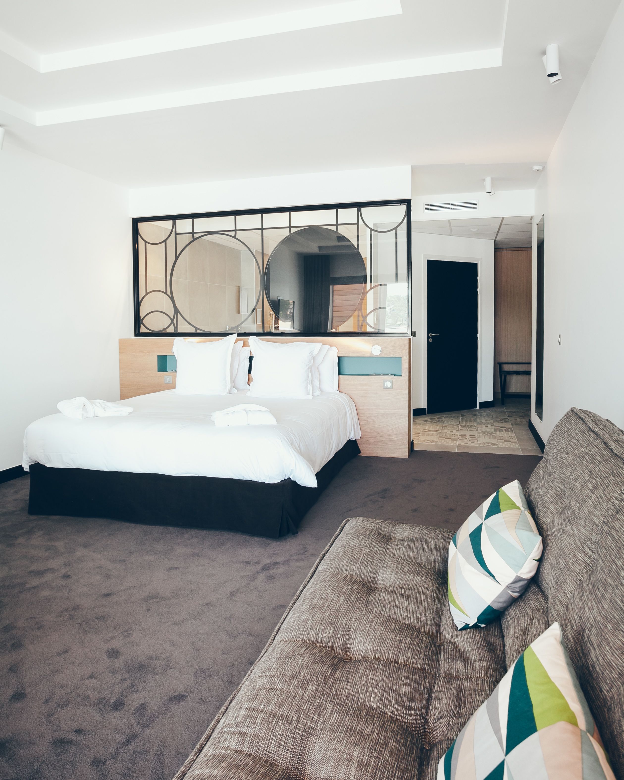 A modern hotel room with a large bed, a sofa, and a mirror above the bed.