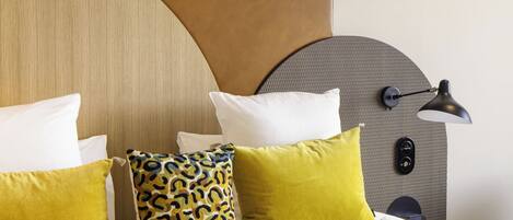 Una cama bien hecha con sábanas blancas y varios almohadones, incluyendo uno amarillo.