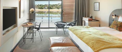 Une chambre d’hôtel moderne dotée d’un grand lit, d’un bureau, d’une chaise et offrant une vue sur un plan d’eau grâce à une porte coulissante.