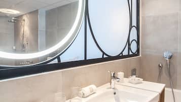 A modern bathroom with a large mirror, a long sink, and a shower area.