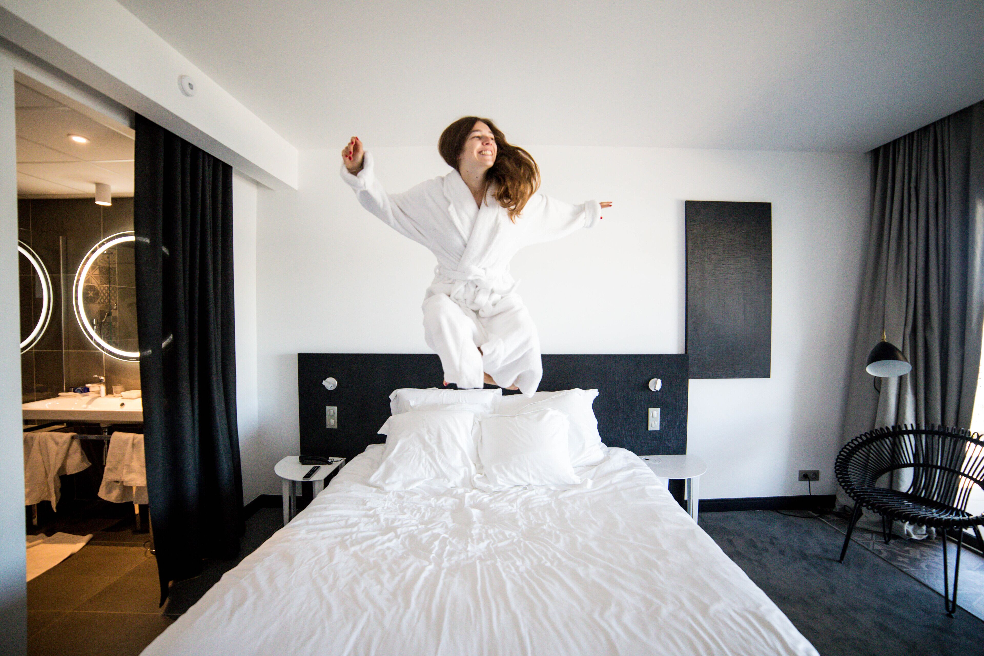 Une chambre d’hôtel avec un lit, un miroir, une chaise et une salle de bain visible au fond.