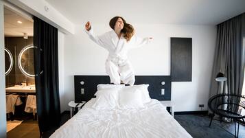 Une chambre d’hôtel avec un lit, un miroir, une chaise et une salle de bain visible au fond.