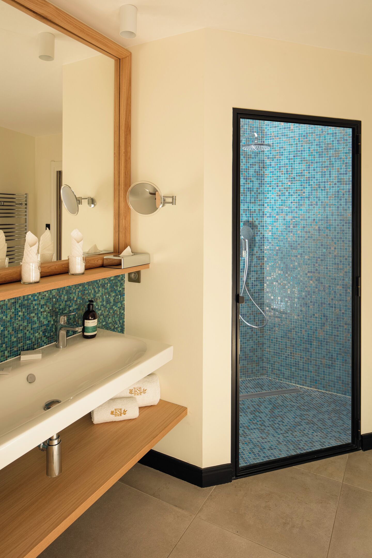Un baño con lavamanos, espejo, toallero y ducha con pared de azulejos.