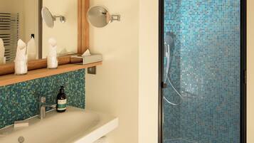Un baño con lavamanos, espejo, toallero y ducha con pared de azulejos.