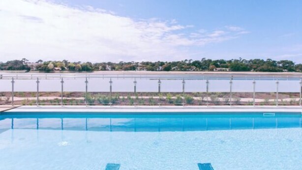 Una piscina rectangular con agua cristalina y azul, rodeada por una barandilla metálica.