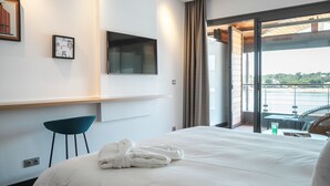 Habitación de hotel con una cama, un televisor de pantalla plana, una silla y vista a un cuerpo de agua a través de una puerta corrediza de vidrio.