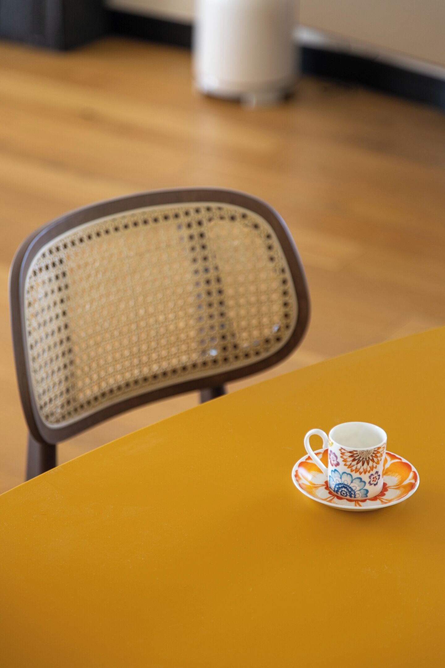 A chair with a woven backrest and a table with a cup and saucer.