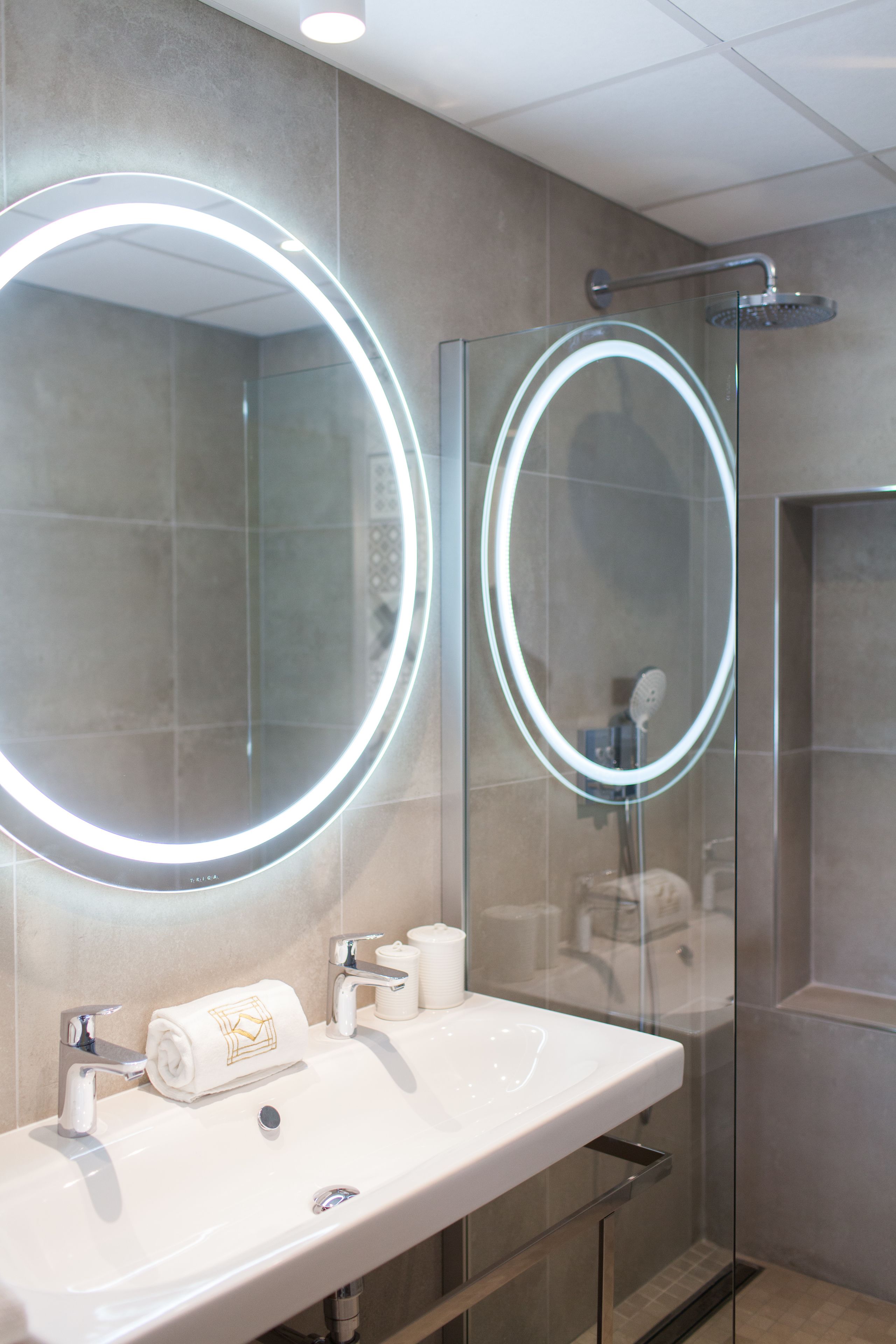 A bathroom with a round mirror, a sink, and a glass-enclosed shower.