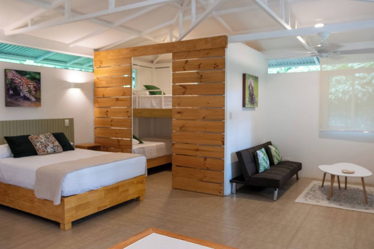 Ein modernes Zimmer mit einem hölzernen Bett, einer Couch und einem kleinen Tisch. Es gibt eine Holzwand und ein Fenster mit Blick.
