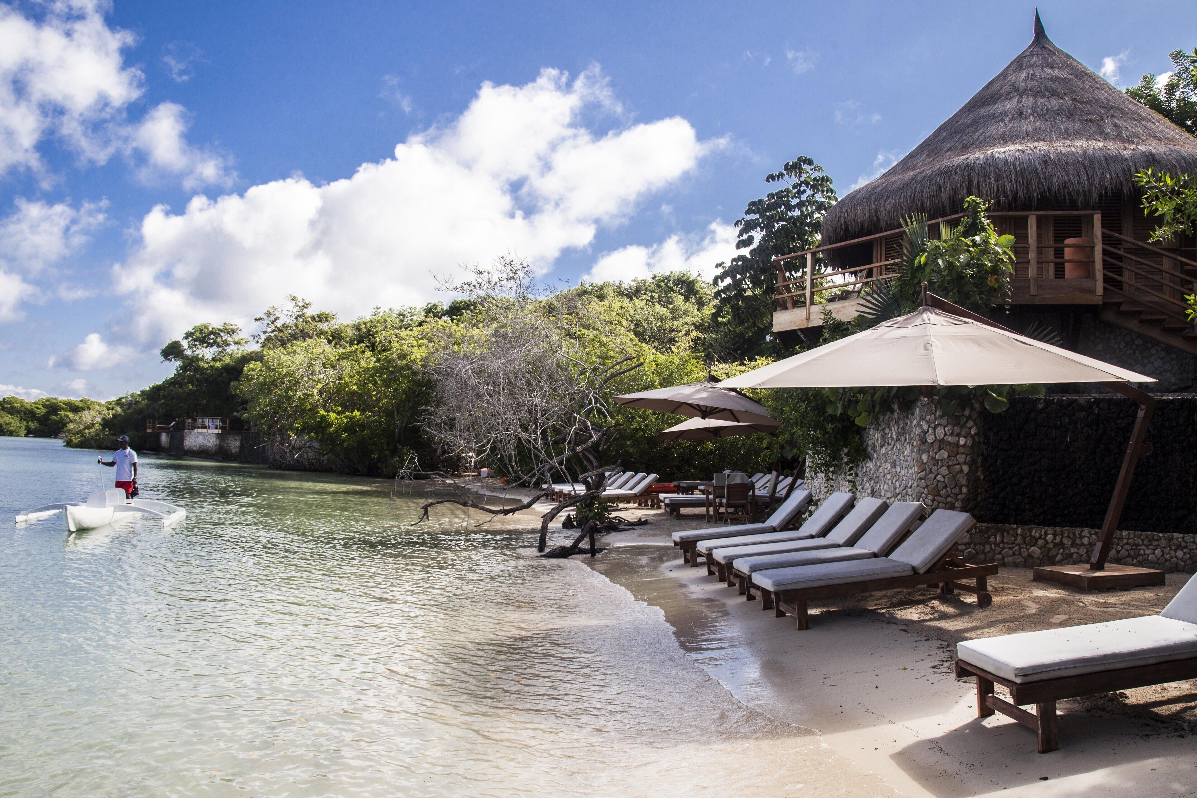 A beachside resort with a thatched-roof building, lounge chairs, and a pool area.