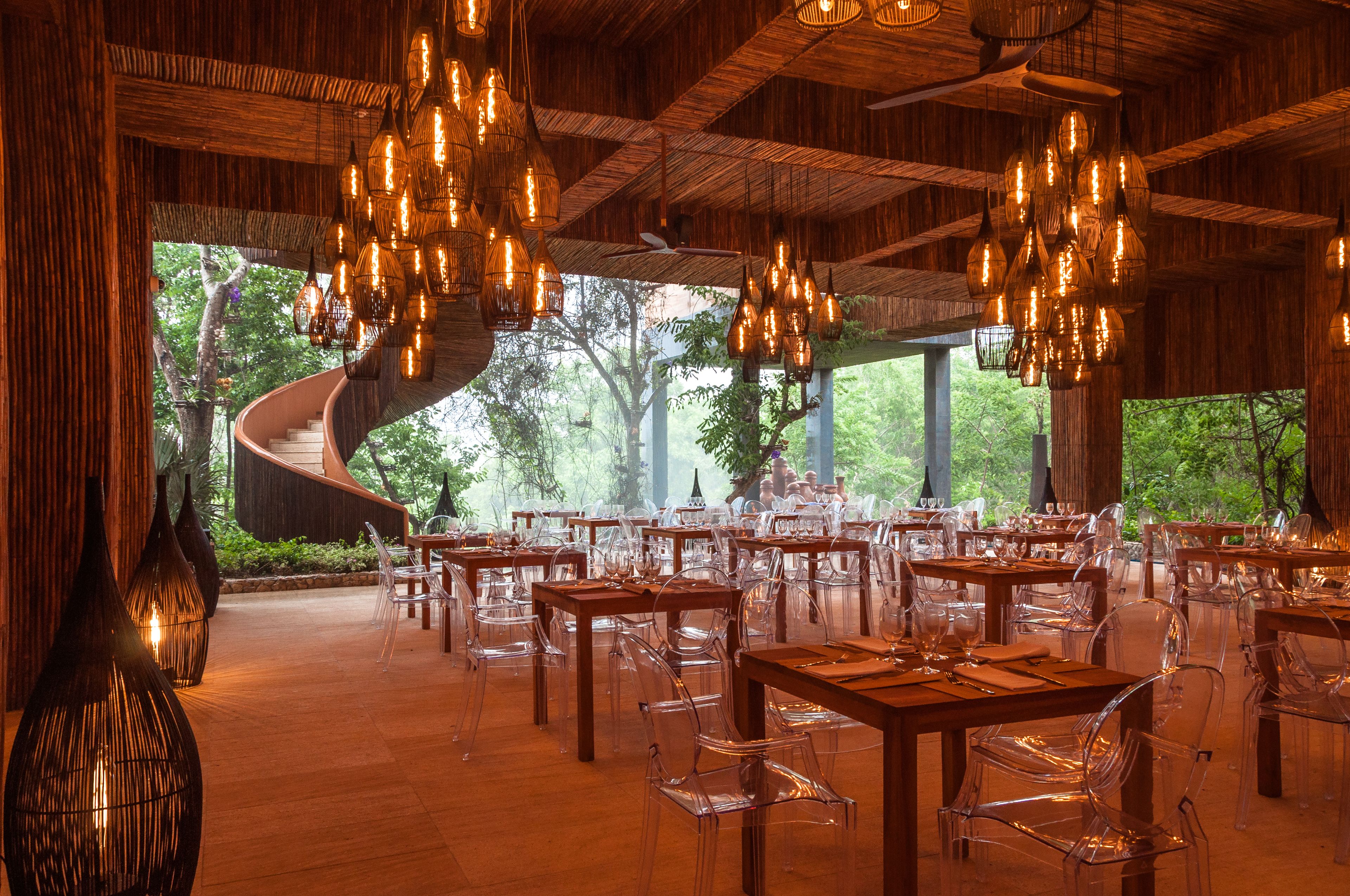 Un restaurante con sillas transparentes, mesas de madera y luces colgantes.