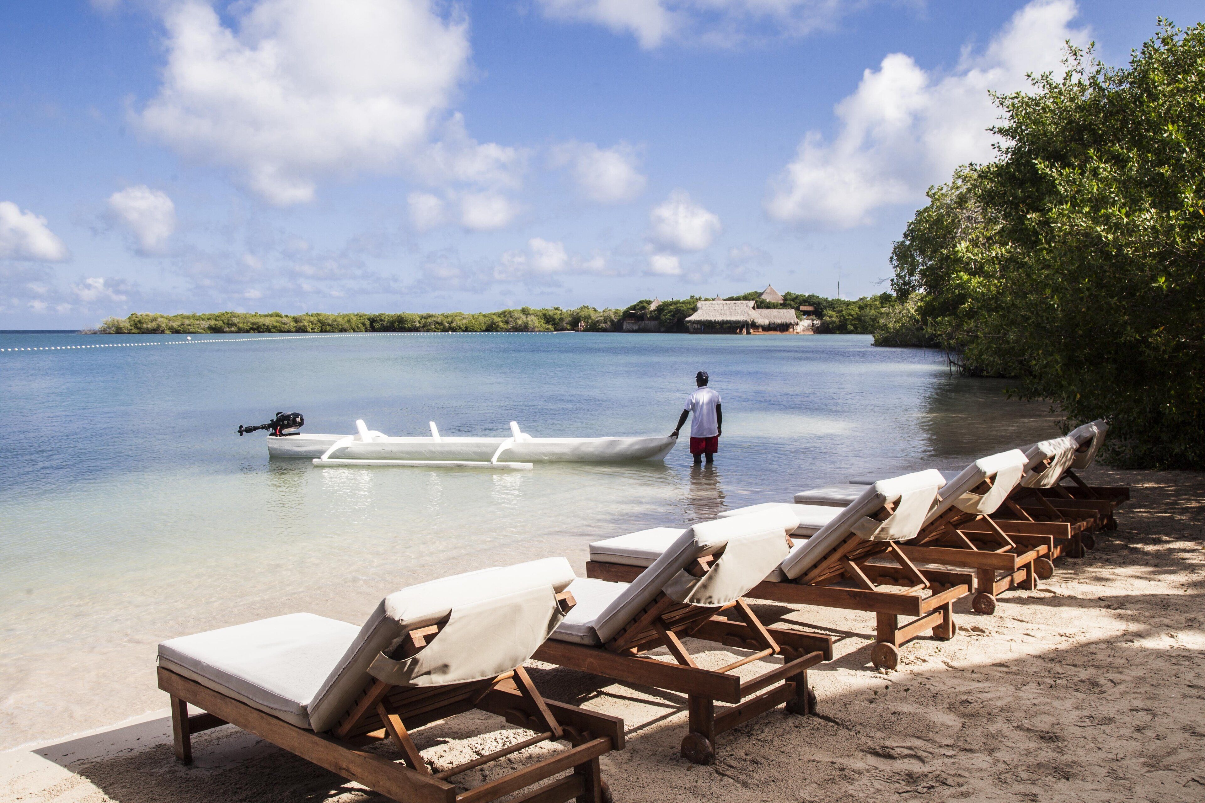 A beach with wooden lounge chairs and a person standing by the water.