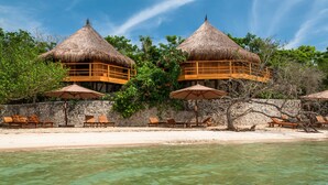 A beachfront resort with thatched-roof bungalows, clear turquoise water, and wooden lounge chairs. - Las Islas (Cartagena)