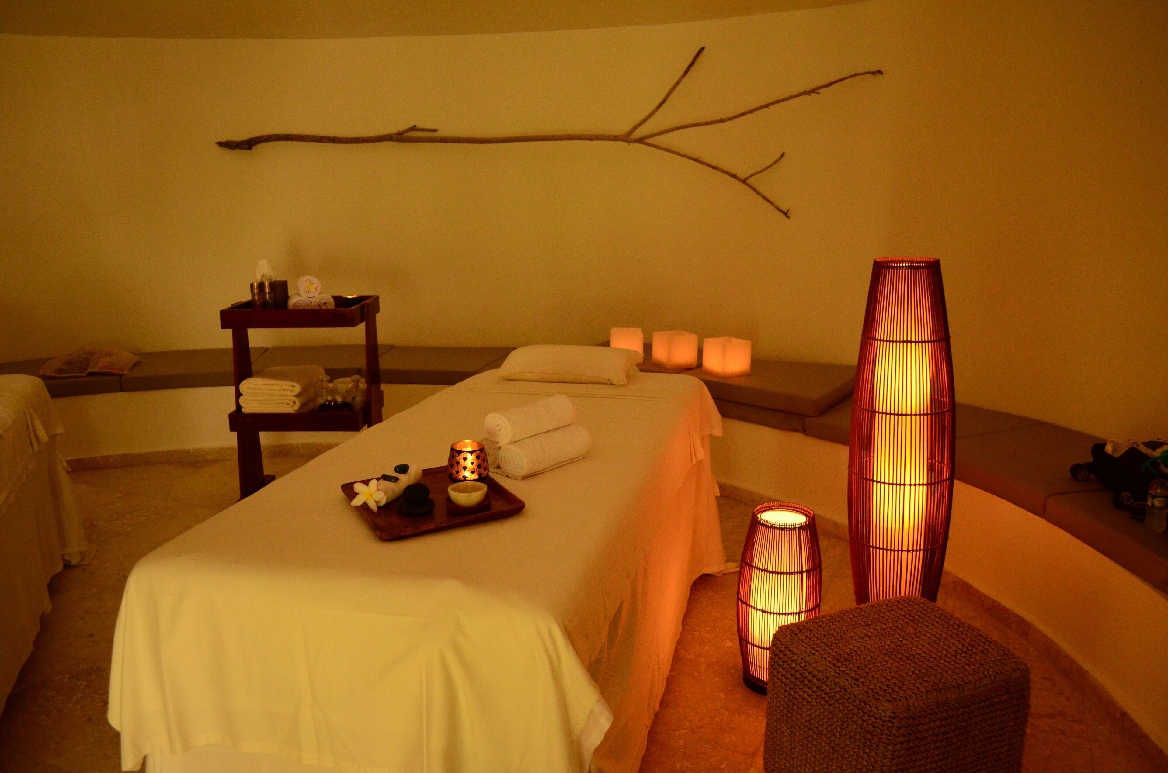 Un cuarto de spa con una camilla de masaje, toallas, velas y una rama decorativa en la pared.